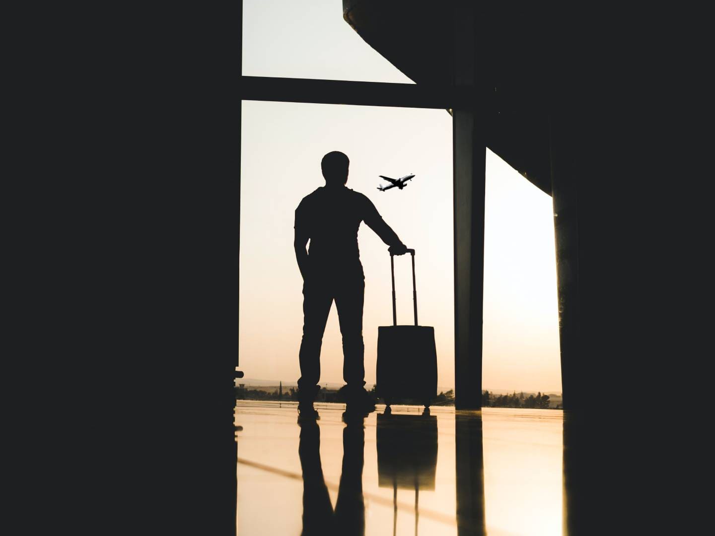 A man standing in front of an airport window with luggage.